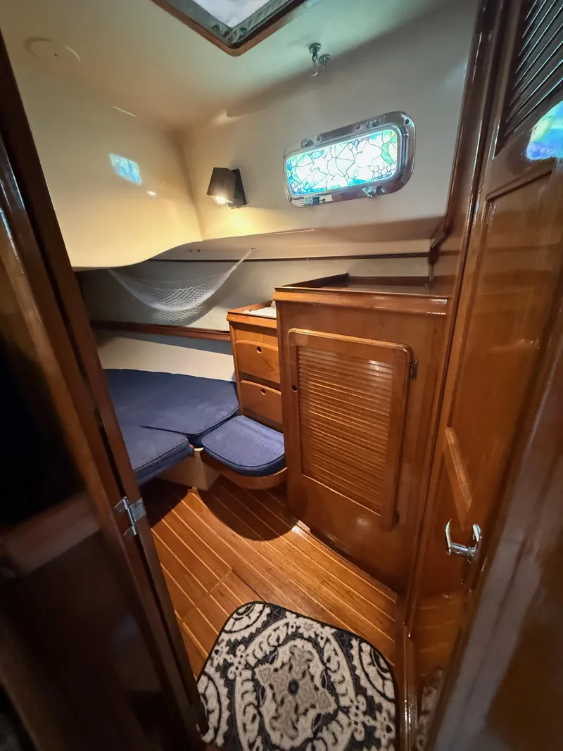 Slide: The Image of 1987 Island Packet 38 cabin interior with wooden finish, blue cushions, and decorative window. - 22