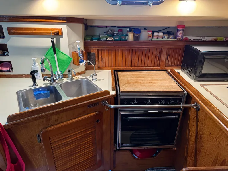 Slide: The Image of 1987 Island Packet 38 yacht kitchen with sink, stove, and wooden cabinetry. - 30