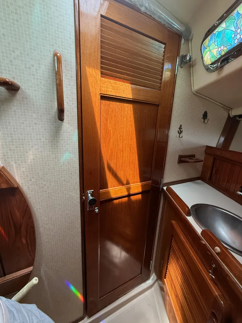 Slide: The Image of Interior of 1987 Island Packet 38 sailboat, featuring wooden cabinetry and a stained glass window. - 45