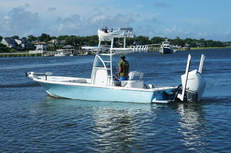 Slide: The Image of 2020 Canyon Bay 24H boat cruising on a scenic river with houses in the background. - 2