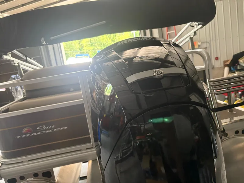 Slide: The Image of 2023 Sun Tracker PB 18 DLX pontoon boat with Mercury outboard motor in a garage. - 2