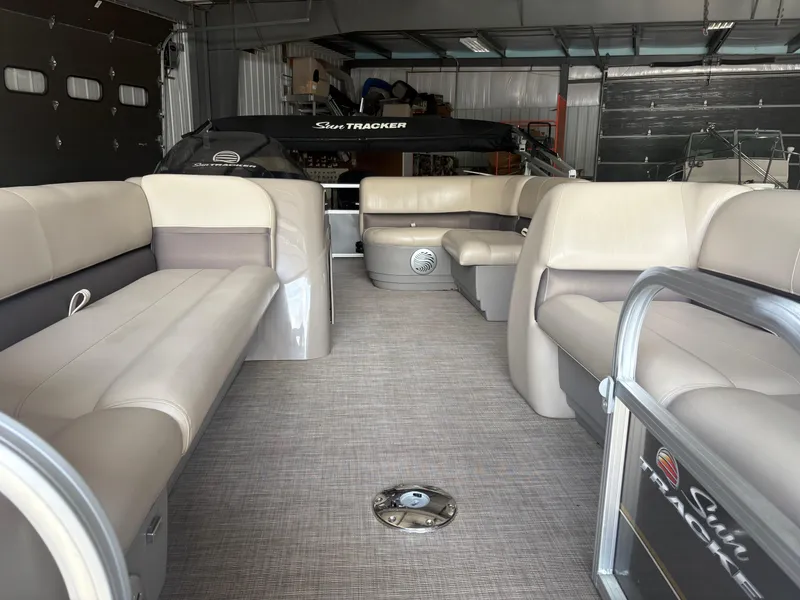 Slide: The Image of 2023 Sun Tracker PB 18 DLX pontoon boat interior with beige seating in a garage. - 5