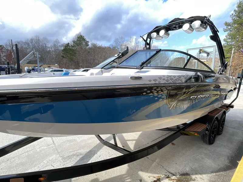 Slide: The Image of 2011 Nautique Super Air Nautique 230 boat on trailer, blue and white design, outdoor setting. - 11