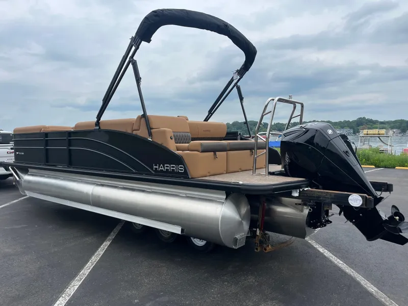 Slide: The Image of 2026 Harris Cruiser 230 pontoon boat with black exterior and tan seating, parked near a lake. - 10