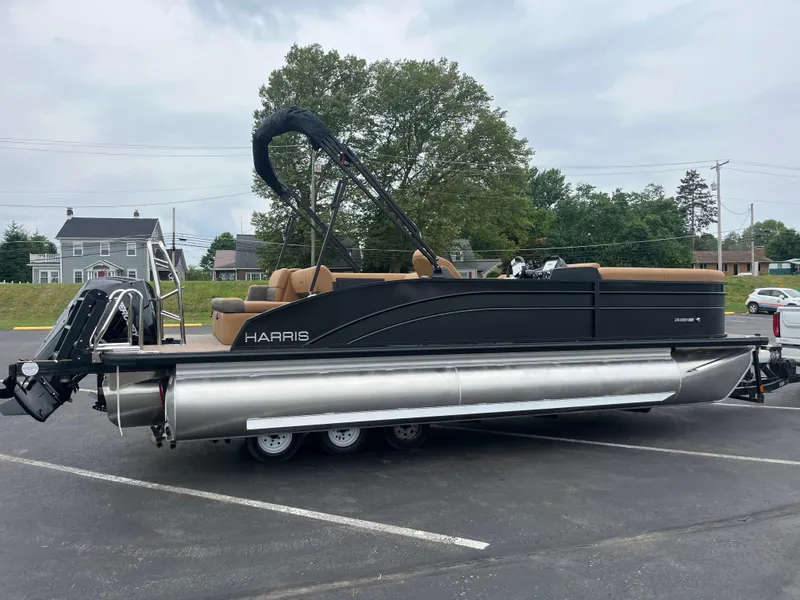 Slide: The Image of 2026 Harris Cruiser 230 pontoon boat on trailer, parked in a lot with trees and houses. - 2