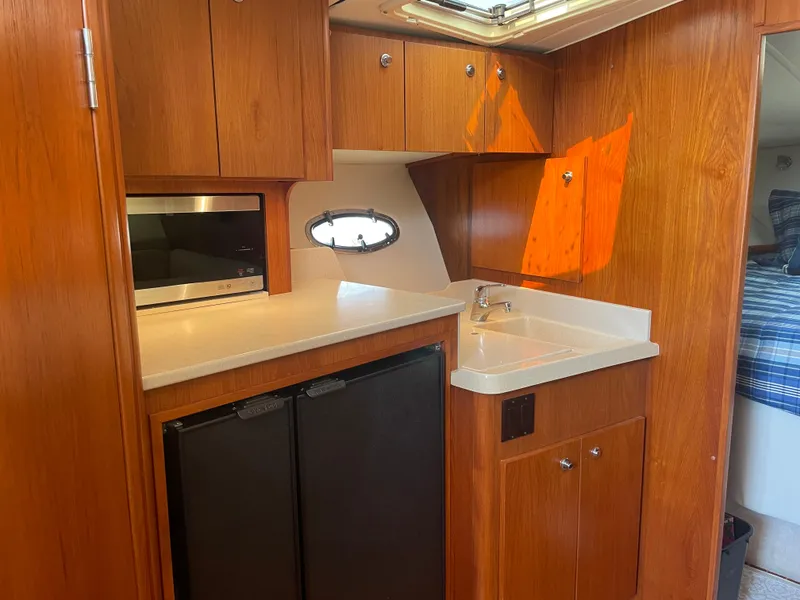 Slide: The Image of 1998 Tiara Yachts 3500 Open galley with wood cabinetry, sink, microwave, and compact refrigerator. - 29