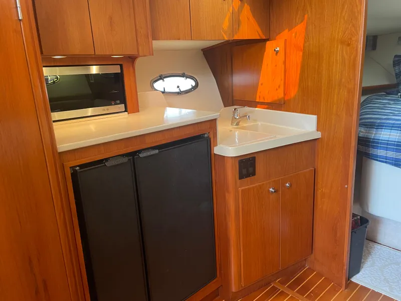 Slide: The Image of 1998 Tiara Yachts 3500 Open interior with kitchenette, featuring wood cabinetry and compact appliances. - 30