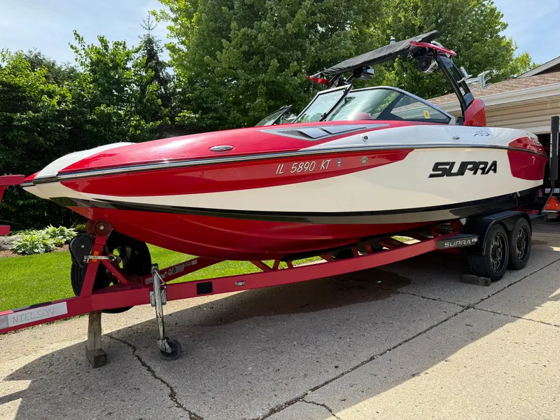 The Image of 2015 Supra SE450-550 boat on trailer, red and white design, parked outdoors. - 1