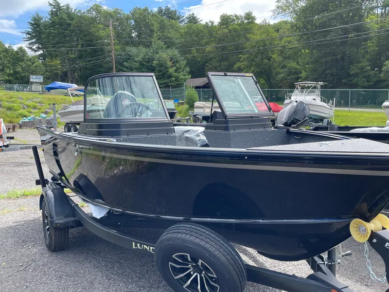 Slide: The Image of 2026 Lund 1800 Explorer Sport boat on trailer, parked outdoors with trees in background. - 8