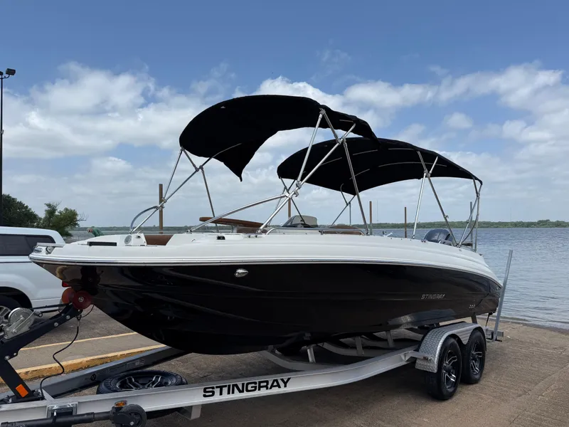 Slide: The Image of 2022 Stingray 212 SC boat on trailer by the water, featuring black hull and canopy. - 0