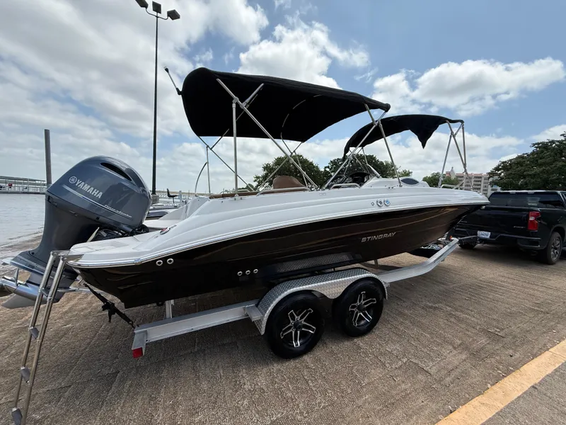 Slide: The Image of 2022 Stingray 212 SC boat on trailer with Yamaha engine, parked near water. - 2