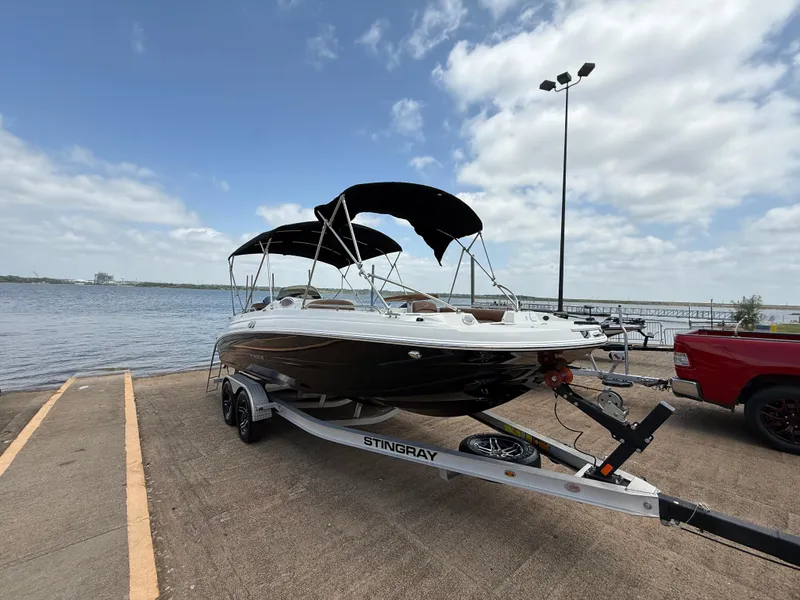 Slide: The Image of 2022 Stingray 212 SC boat on trailer by waterfront under cloudy sky. - 3