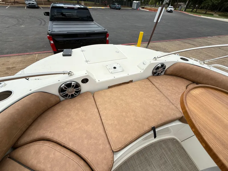 Slide: The Image of 2022 Stingray 212 SC boat interior with tan seating and wooden table, parked near a Chevrolet Silverado. - 44