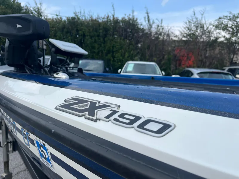 Slide: The Image of 2018 Skeeter ZX190 boat with logo, parked outdoors, surrounded by cars and trees. - 21