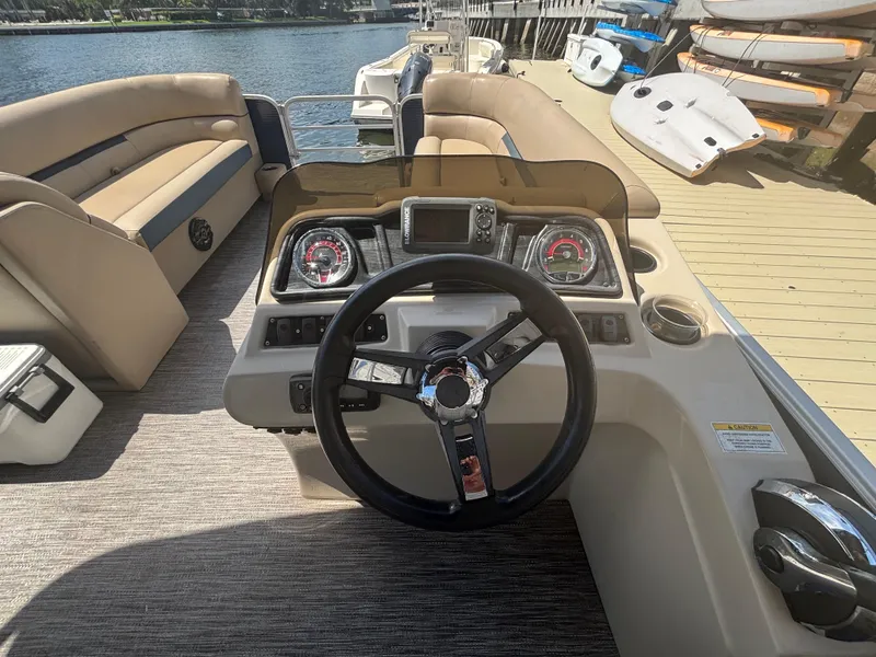 Slide: The Image of 2021 Godfrey Sweetwater boat dashboard with steering wheel and gauges, docked by the water. - 16