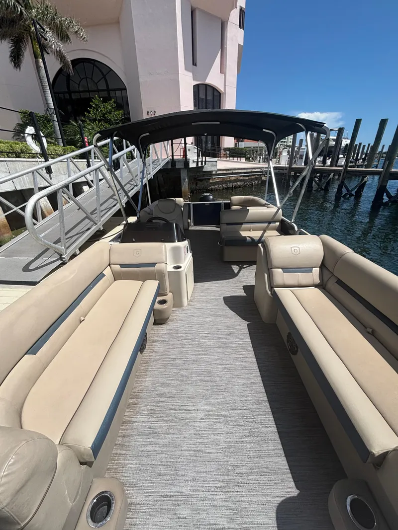 Slide: The Image of 2021 Godfrey Sweetwater pontoon boat docked by a waterfront building under clear blue skies. - 9