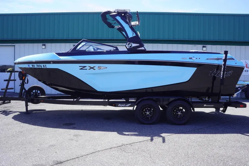 Slide: The Image of 2023 Tigé 23ZX boat on trailer, blue and black design, parked outdoors. - 0