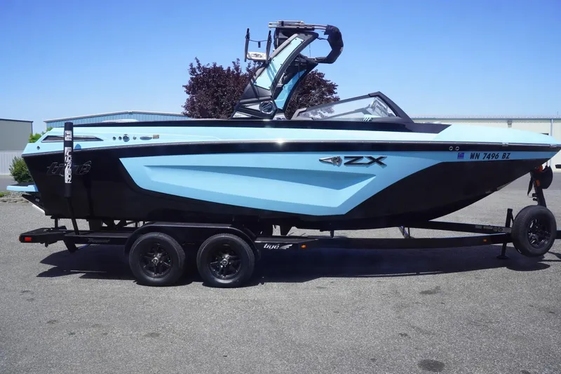 Slide: The Image of 2023 Tigé 23ZX boat on trailer, light blue and black design, parked outdoors. - 1