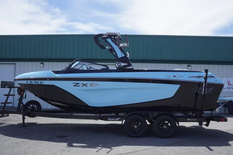 Slide: The Image of 2023 Tigé 23ZX boat on trailer, parked outside a green-roofed building. - 2