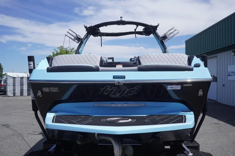 Slide: The Image of 2023 Tigé 23ZX boat, rear view, blue and black design, parked outdoors. - 25