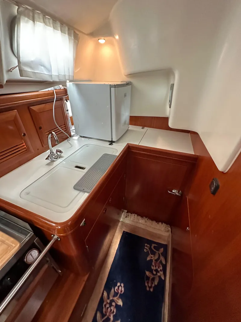 Slide: The Image of 2002 Beneteau 411 yacht kitchen with wood cabinetry, compact fridge, and sink. - 32