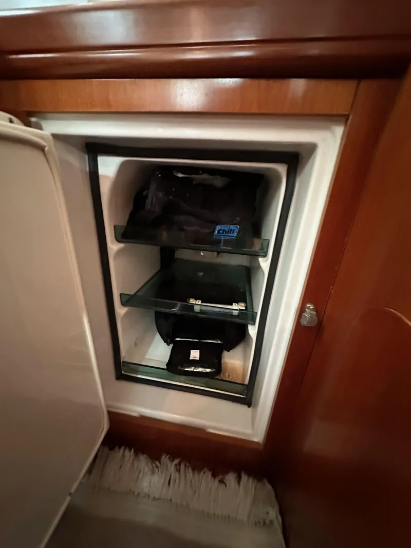 Slide: The Image of Mini fridge inside 2002 Beneteau 411 yacht, featuring wooden cabinetry and compact storage shelves. - 33