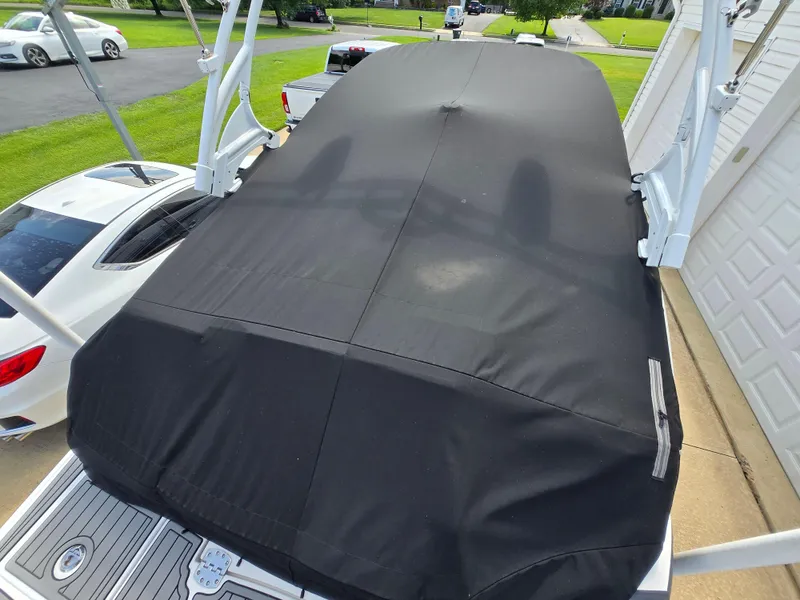 Slide: The Image of Covered 2021 Monterey M-65 boat parked near a garage, with cars in the background. - 27