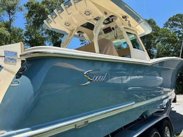 Slide: The Image of 2018 Scout 355 LXF boat in blue, docked outdoors with trees in the background. - 13