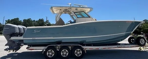 Slide: The Image of 2018 Scout 355 LXF boat on trailer, parked on grass with trees in background. - 6