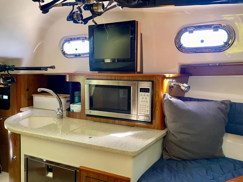 Slide: The Image of 2011 Pursuit 315 Offshore cabin with kitchenette, microwave, TV, and seating area. - 43