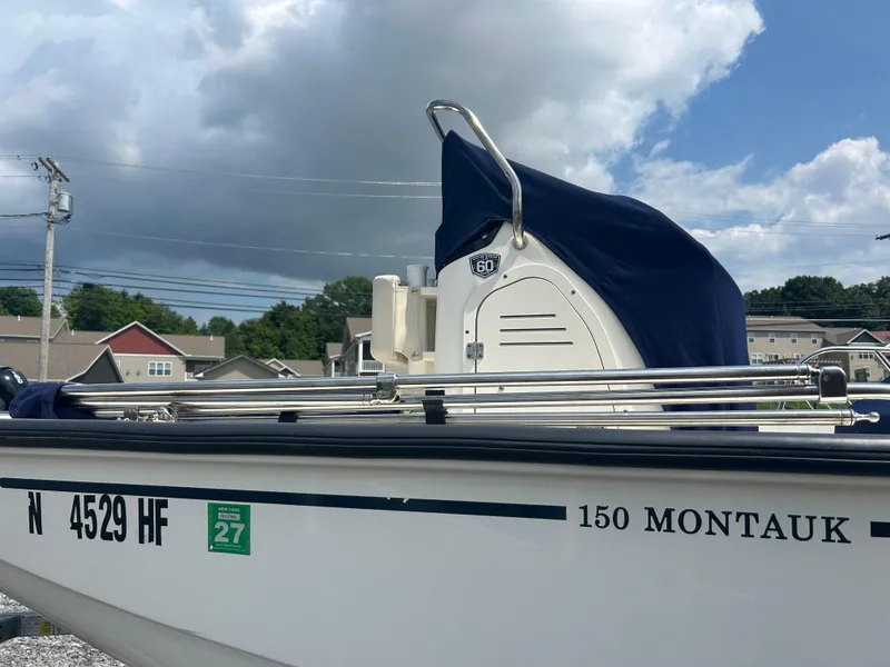 Slide: The Image of 2018 Boston Whaler 150 Montauk boat with cover, parked outdoors under cloudy sky. - 3