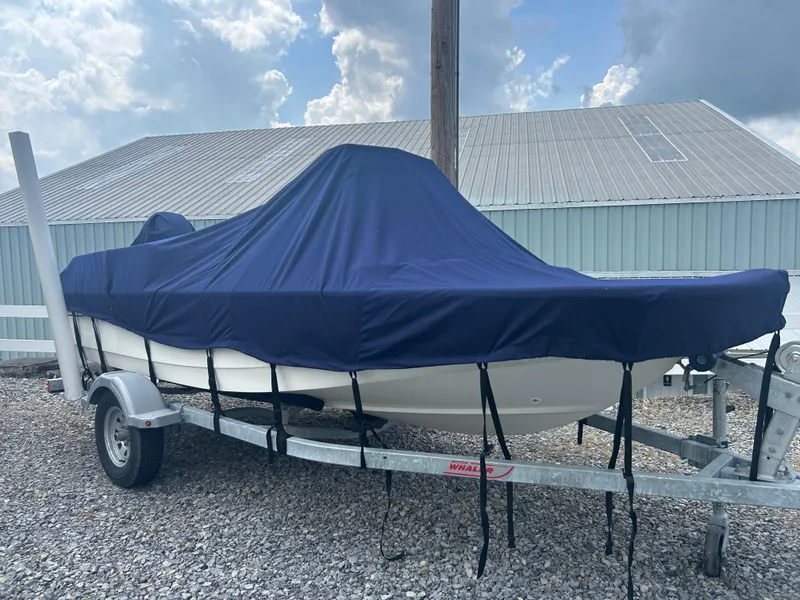 Slide: The Image of 2018 Boston Whaler 150 Montauk on trailer, covered with blue tarp, parked outdoors. - 7