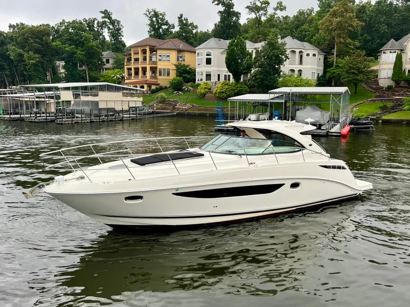 Slide: The Image of 2014 Sea Ray 410 Sundancer yacht cruising on a scenic lake near luxury homes. - 2