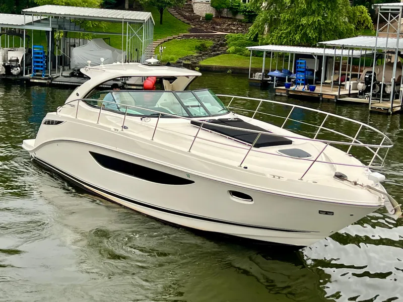 Slide: The Image of 2014 Sea Ray 410 Sundancer yacht cruising on a calm lake near docks. - 6
