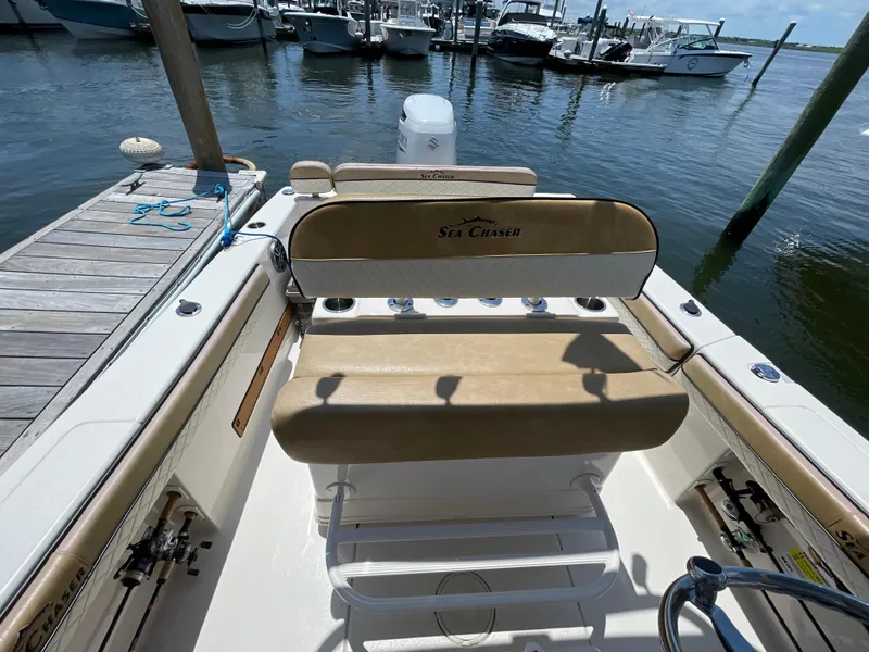 Slide: The Image of 2023 Sea Chaser 24 HFC boat interior at dock, featuring tan seating and fishing rod holders. - 22