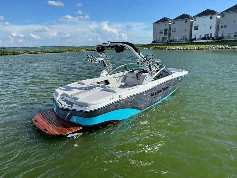 Slide: The Image of 2019 MasterCraft XT22 boat on a lake near modern homes under a blue sky. - 6