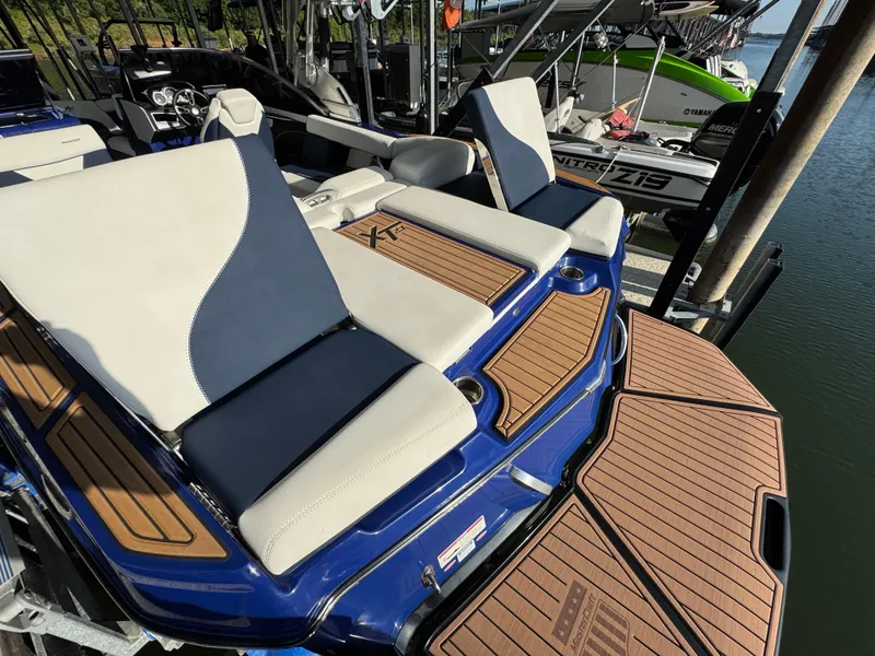 Slide: The Image of 2021 MasterCraft XT23 boat with cushioned seating and teak flooring, docked by the water. - 10
