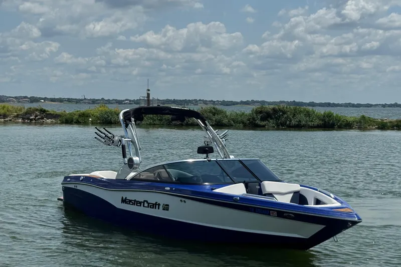 Slide: The Image of 2021 MasterCraft XT23 boat on a calm lake under a cloudy sky. - 2