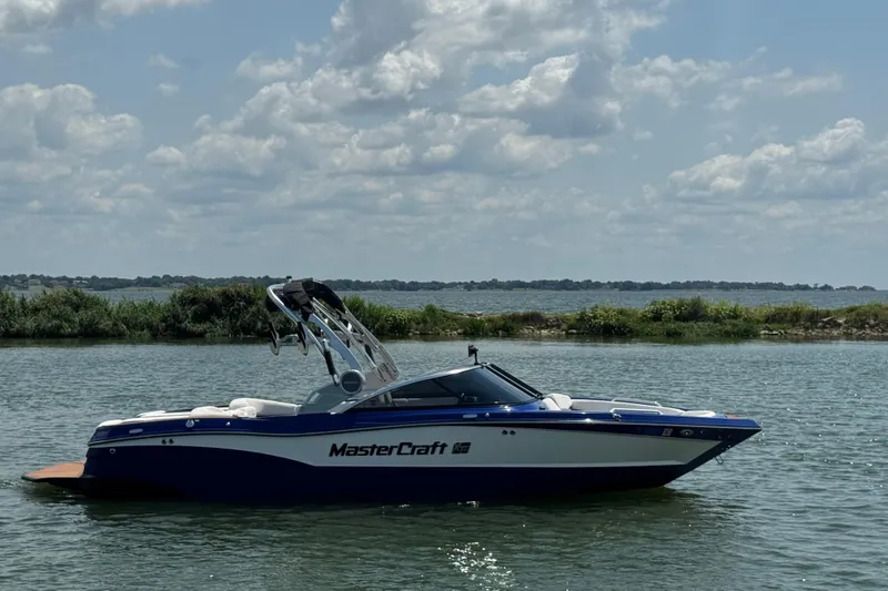 Slide: The Image of 2021 MasterCraft XT23 boat on a calm lake under a cloudy sky. - 3