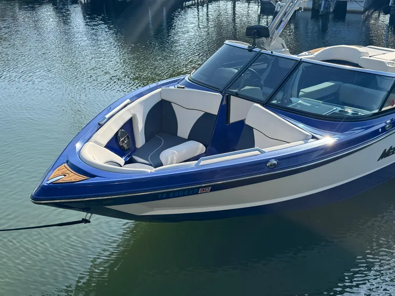 Slide: The Image of 2021 MasterCraft XT23 boat with blue and white design, docked on calm water. - 4