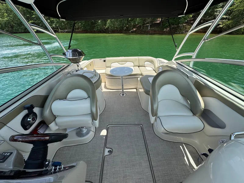 Slide: The Image of 2006 Sea Ray 270 Sundeck interior with seating, table, and steering wheel on a lake. - 28