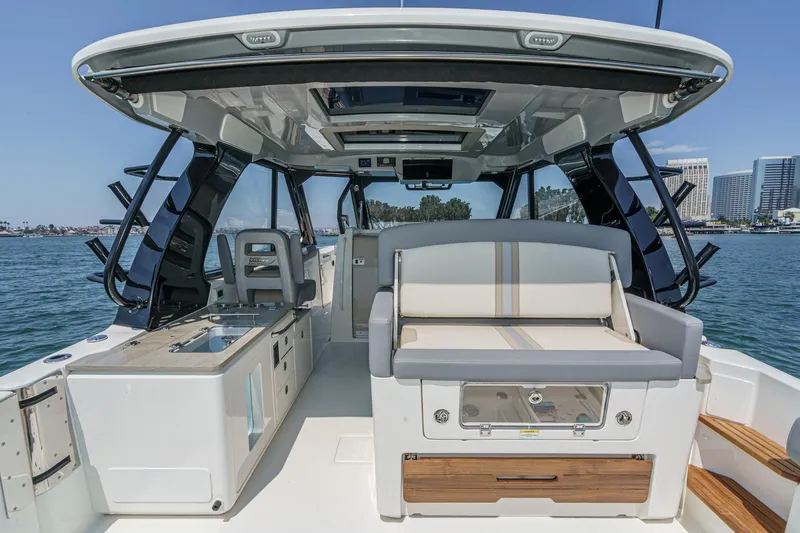 Slide: The Image of 2024 Boston Whaler 380 Realm boat interior with seating and kitchenette, docked near cityscape. - 52