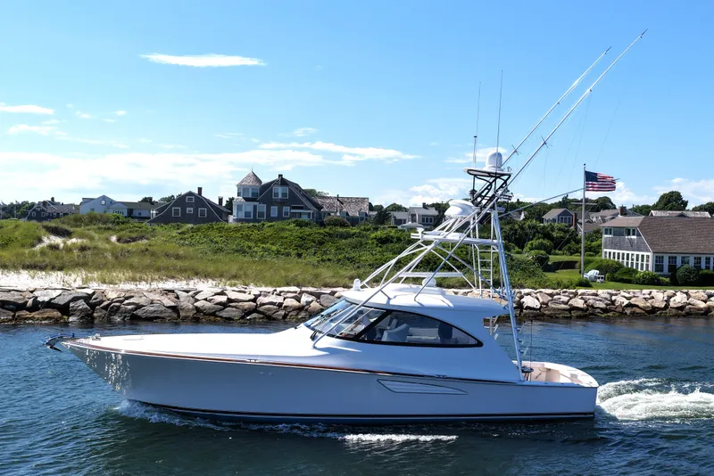 Slide: The Image of 2024 Viking 48 Sport Tower yacht cruising near coastal homes under a clear blue sky. - 26
