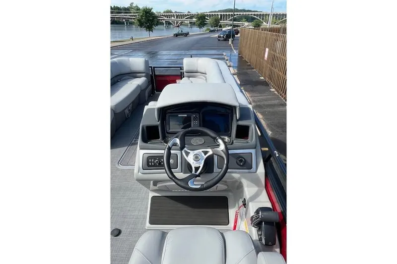 Slide: The Image of 2024 Regency 250 DL3 pontoon boat interior with steering wheel and seating, docked by a river. - 14
