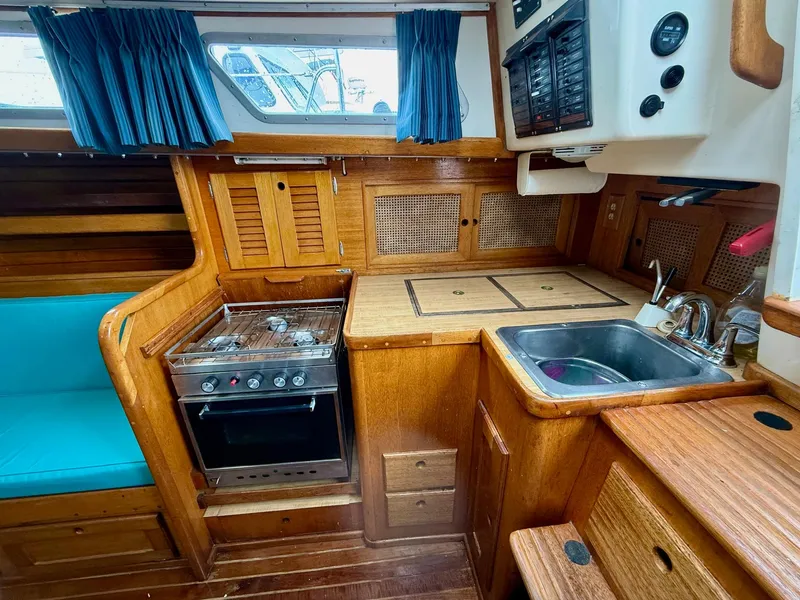Slide: The Image of 1981 Bristol 35.5 yacht interior with wooden cabinetry, stove, sink, and blue curtains. - 7