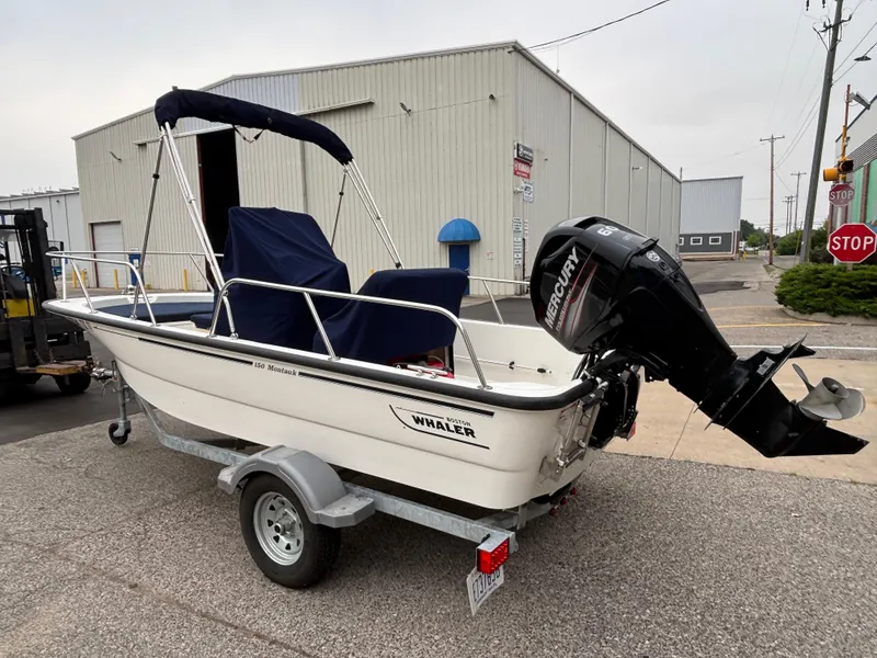 Slide: The Image of 2016 Boston Whaler 150 Montauk boat with Mercury engine on trailer, parked near industrial building. - 5