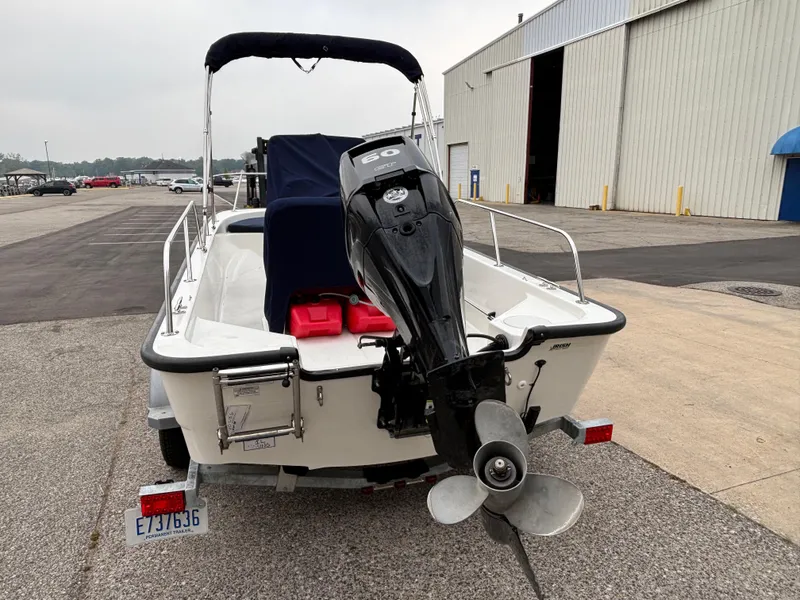 Slide: The Image of 2016 Boston Whaler 150 Montauk boat with outboard motor, parked near a large warehouse. - 6