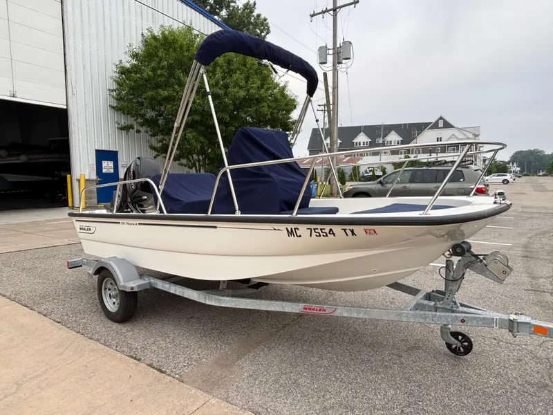 Slide: The Image of 2016 Boston Whaler 150 Montauk boat on trailer, parked near a building. - 8