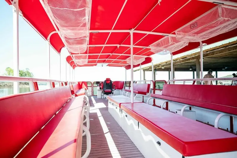 Slide: The Image of 2024 Aloha Pontoon 50' Water Taxi with red seating and canopy, docked by the water. - 11