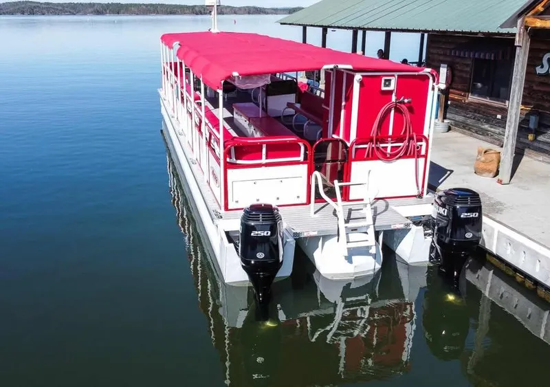 Slide: The Image of 2024 Aloha Pontoon 50' Water Taxi with red canopy docked on calm water. - 2
